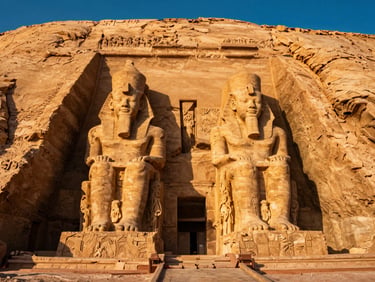 Temple of Abu Simbel at golden hour, massive stone statues of Ramesses II carved into the mountainside, warm sunlight, dramatic shadows.