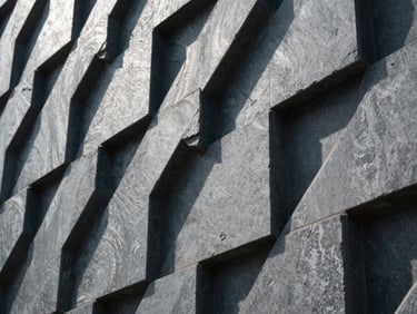 Macro perspective of a highly structured modern architectural facade, sharp linear shadows, cool daylight, high contrast, slate grey tones.