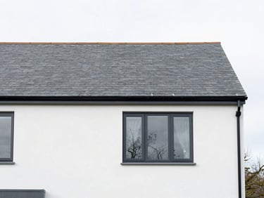 Medium shot of a clean modern Devon home exterior with slate roofing, bright overcast daylight, sharp focus, 35mm lens
