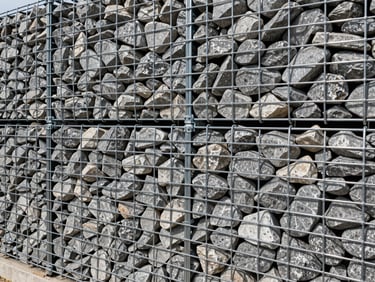 Close-up of a double-twisted wire mesh gabion box tightly packed with angular grey river stones, structural retaining wall application, daylight.