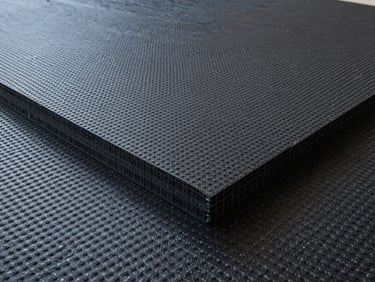 Technical detail of a drainage composite sheet, showing the dimpled plastic core laminated with a non-woven geotextile filter, clean studio lighting.