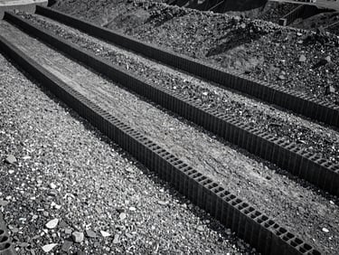 High-angle view of a three-dimensional honeycombed geocell confinement system filled with crushed aggregate on a sloped embankment, sharp focus.