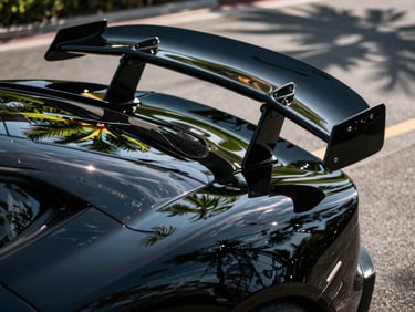 Low-angle close-up of a black exotic sports car wing, deep glossy reflections of palm trees, sharp highlights, 50mm lens