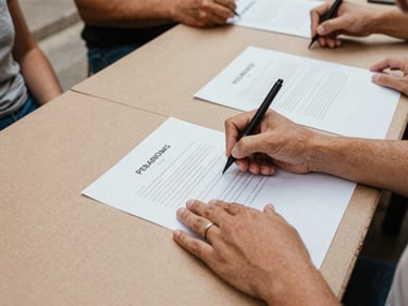 A close-up of hands writing proposals on a large paper board during a community assembly, warm natural light, 35mm