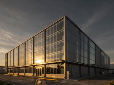 Editorial architectural photography of a cutting-edge logistic facility exterior, steel and glass structure, dramatic high-contrast sky, golden hour.