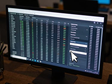 Close overhead shot of a wide monitor displaying a live native ad campaign dashboard, rows of real-time bid data and CTR columns illuminated by cool screen glow, a cursor mid-hover over a targeting parameter dropdown, dark ambient office surroundings, no visible face
