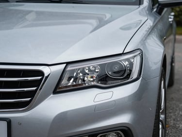 Close-up of a clean silver sedan headlight and grille, parked on clean pavement, sharp focus, professional lighting.