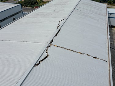 Aerial inspection drone view over a large industrial roof structure showing cracks and surface deterioration mapped from above, sharp detail on surface condition, overcast natural light, no people visible
