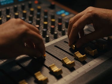 Macro shot of hands adjusting gold faders on a vintage analog mixing console, low-key lighting, warm amber glow, 35mm film.