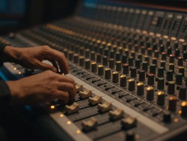 Cinematic film still, moody low-key lighting, hands adjusting a massive analog mixing console, warm amber glow on faders, shallow depth of field