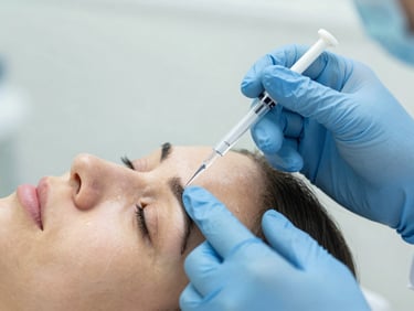 Macro shot of Dr. Joi Johnson's hands demonstrating a precise injection technique on a live model's forehead, focus on needle placement, bright diffused daylight, soft teal and slate accents, crisp focus, high-end medical aesthetic, 35mm.