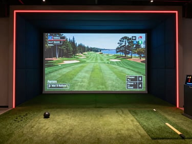 Wide shot of a premium indoor golf simulator screen displaying Pebble Beach golf course. Neon red accent lines framing the enclosure, deep midnight blue shadows, high-fidelity projection.