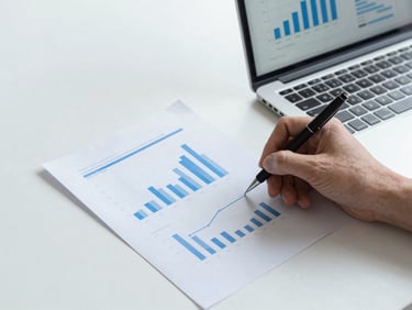 Hands writing notes next to a laptop displaying clean statistical graphs, warm daylight, minimalist