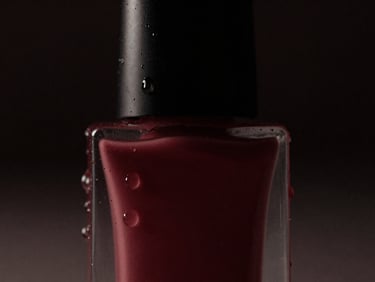 Moody cinematic close-up of a premium cosmetic bottle with water droplets, dramatic low-key studio lighting, deep shadows, dark charcoal and wine-red tones, 35mm