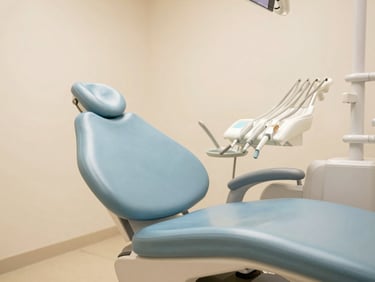 Wide shot of a light-filled, clean dental treatment room, soft Baltic blue and sandy cream tones, comfortable patient chair, no visible instruments, warm natural light.