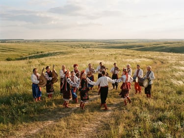 Wide-angle outdoor performance of Ukrainian folk ensemble in authentic embroidered costumes standing in the middle of a vast wild-grass steppe at golden hour, warm late afternoon sunlight, 35mm editorial photography