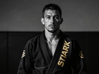 Stark black and white portrait of an athletic male instructor in a black gi, looking off-camera, high-contrast athletic lighting.