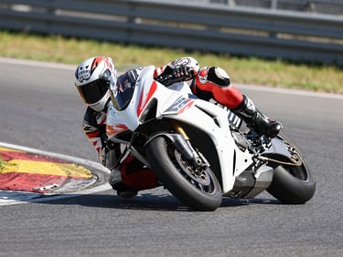 Low-angle wide dynamic shot of a superbike leaning deep into turn four under harsh midday sun, knee slider scraping the high-friction asphalt, motion blur on the background.