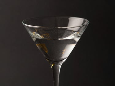 Close-up of a sleek, minimalist martini glass, empty, catching dramatic rim light, dark charcoal background, gold reflections, 85mm lens