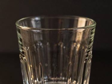 Close-up of an intricate textured highball glass, empty, catching dramatic rim light, dark charcoal background, gold reflections, 85mm lens