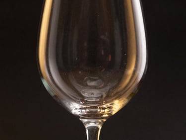 Close-up of a pristine, elegant red wine glass, empty, catching dramatic rim light, dark charcoal background, gold reflections, 85mm lens