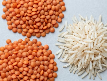 Overhead flat-lay of sorted red lentils and long-grain Basmati rice on a clean light grey surface, sharp focus