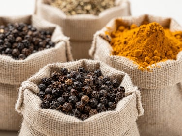 Close-up shot of raw black pepper and turmeric powder in clean burlap sacks, bright natural daylight, sharp focus