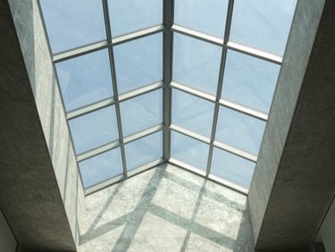 Interior view of a massive geometric glass skylight, clean structural steel lines casting sharp shadows on concrete walls.
