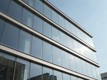 Low-angle architectural shot of a modern commercial curtain wall facade, clean glass panels reflecting a clear blue sky, crisp shadows.