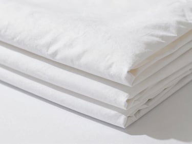 Close-up of crisp, white hotel-grade bed linen, perfectly folded, bright natural daylight, sharp detail.