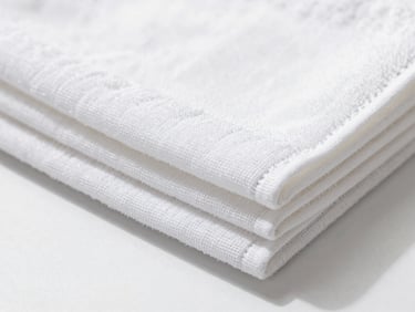 Close-up of a neatly folded, textured white kitchen towel, bright natural daylight, sharp detail.
