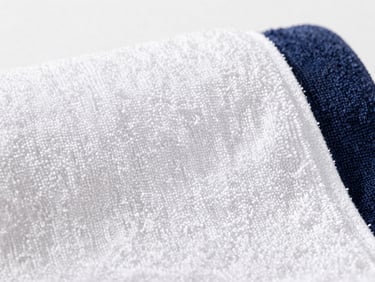 Close-up macro shot of a plush white terry towel, highly absorbent texture visible, bright natural daylight, clean white background.