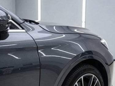 Close-up of a high-end car fender with a flawless, mirror-like dark grey paint finish reflecting bright, linear LED strip lights of an immaculate workshop