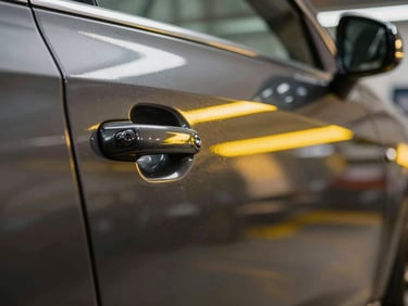 Macro shot of the same dark metallic car door, now perfectly smooth, reflecting perfectly straight, parallel yellow LED lines under bright workshop light.