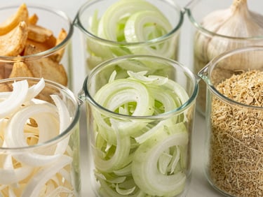 Dehydrated white onion flakes and garlic powder in clean industrial glass beakers, bright natural light, professional food ingredient shot