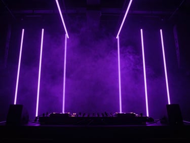 Wide-angle photograph of a modern DJ booth in a dark club environment, vertical purple LED light bars cutting through heavy atmospheric smoke, high contrast, concert lighting