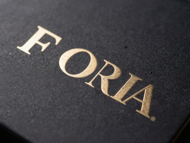 Close-up of premium embossed retail packaging with brushed champagne-gold foil lettering, dark charcoal background, dramatic side lighting.