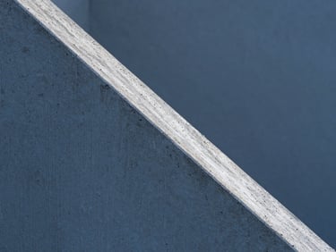 Ultra-tight abstract macro detail of raw concrete texture, a sharp diagonal shadow cutting across the frame, cold clinical blue hour lighting, high-contrast architectural photography, precise geometric lines.
