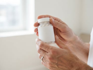Close-up of an active adult's hands gently holding a Re-Life OA supplement bottle, bright natural daylight, soft shadows, minimalist product shot, wide aspect.