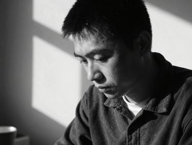 High-contrast black and white portrait of an artisan looking down, heavy shadows, natural light leak, film grain.