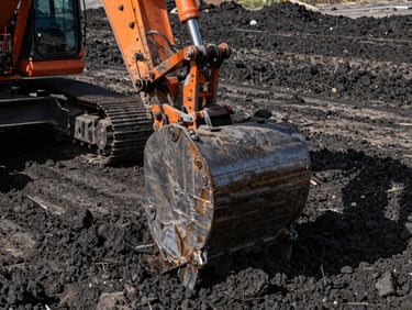 Close-up of a heavy tracked excavator bucket digging into dark soil, sharp industrial lighting, gritty texture, high contrast.