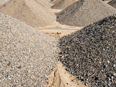 Symmetrically stacked piles of clean, uniform gravel and sand, bright harsh daylight, high contrast warm tones, sharp focus, 35mm, gritty industrial photography