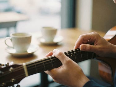 Close up of hands playing an acoustic guitar in a warm-lit cafe, soft focus background with heavy ceramic mugs, warm morning light, 35mm film