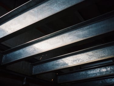 Industrial film photography of heavy structural steel beams, close-up, high-contrast side-lighting, cool metallic tones, sharp focus, 35mm.