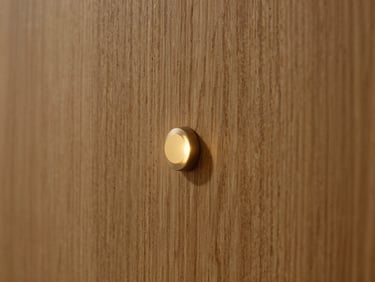 Extreme close-up of a seamless warm oak wall panel with an integrated, completely flush invisible sensor glowing with a micro warm gold light indicator, cinematic shadow
