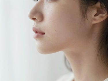 Soft-focus editorial photography of a woman's profile, warm diffused daylight, highlighting natural skin texture and soft jawline, shallow depth of field.