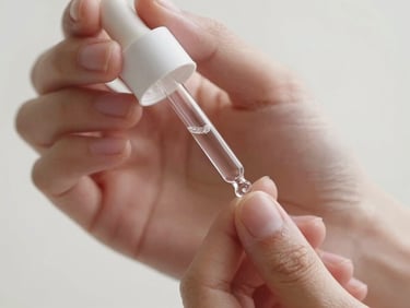 Delicate close-up of clean hands holding a translucent glass dropper with a clear skin serum, warm lighting, minimalist white background.