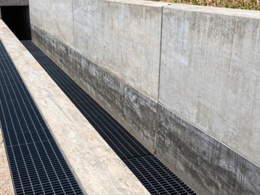 Commercial grade flood barrier and heavy drainage trench installed along a concrete retaining wall, industrial steel grates.