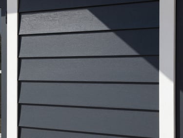 Close-up of premium fiber-cement siding panels installed on a modern farmhouse, clean charcoal-black lines, sharp shadows.