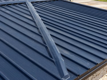 Close-up of a perfectly tensioned standing seam metal roof, deep navy steel panels under bright Texas sunlight, architectural angle.